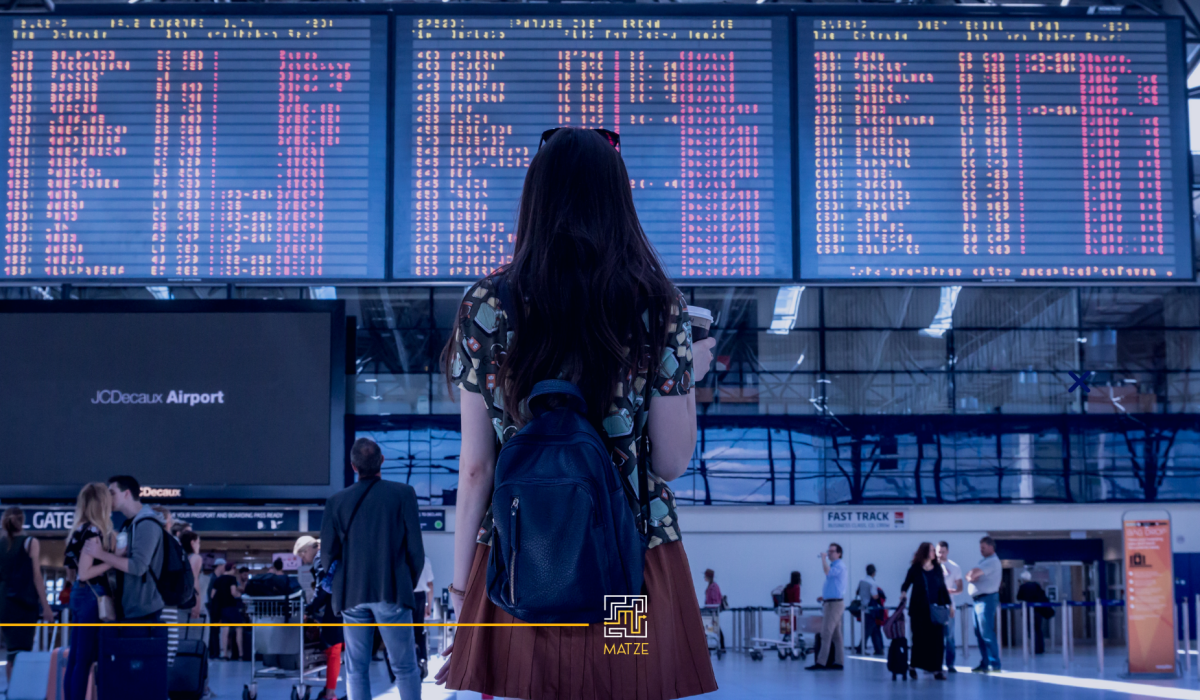 card com foto de uma mulher de costas olhando para o painel de voos do aeroporto. No canto superior direito, num fundo azul, está escrito: "A qualidade no atendimento ao passageiro:", em amarelo; abaixo, em letras brancas, está a continuação do texto: "a experiência do cliente nas companhias aéreas". No rodapé há uma linha amarela com o labirinto branco e a letra "M" em amarelo representando o logotipo da Matze Consultoria