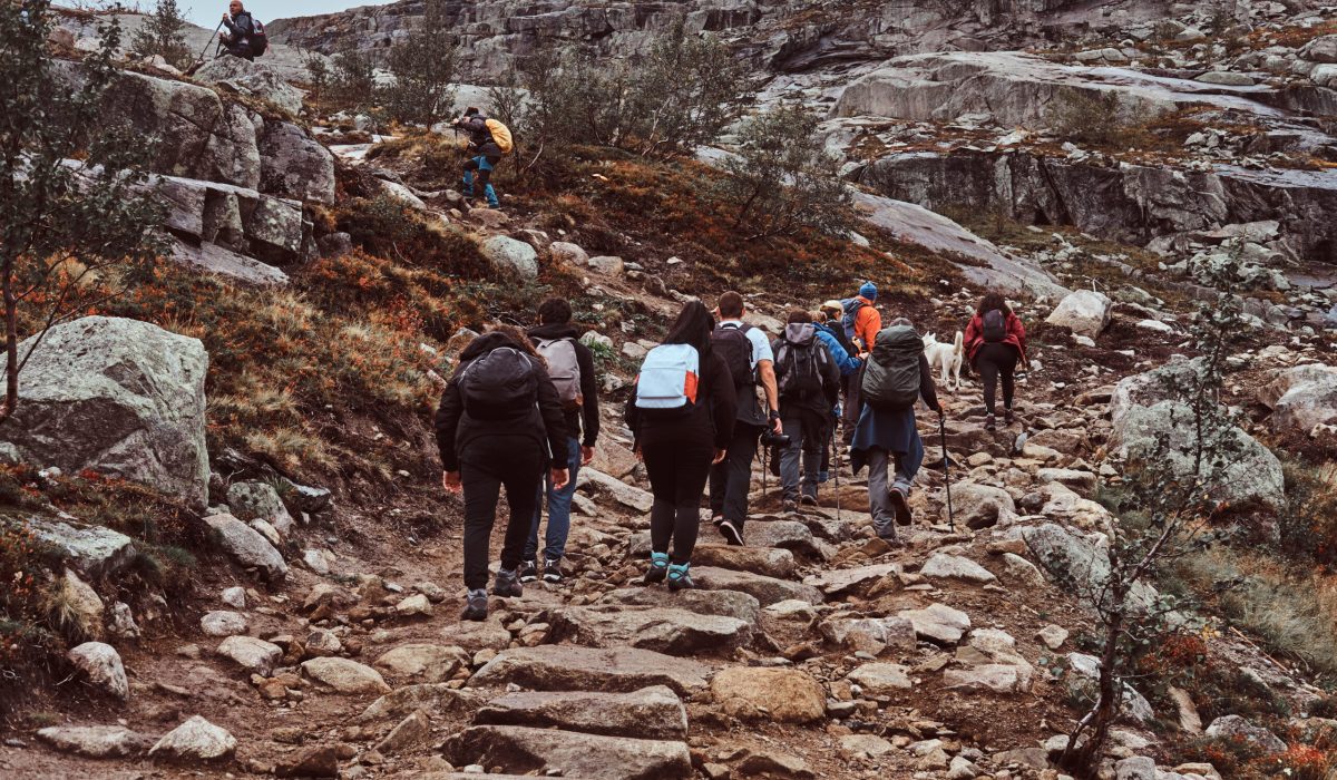 Imagem de um grupo grande de pessoas fazendo trilha com mochilas nas costas nas montanhas.
